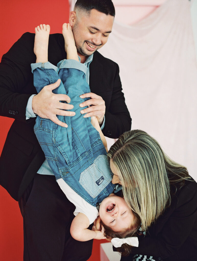 A Dad throws his little girl upside down while mom tickles here, and she laughs gleefully.