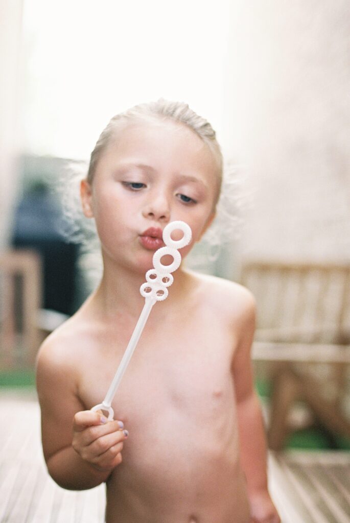A little girl blowing bubbles in her backyard during an in-home family session. One of the many fun ideas for in-home family photos in Frisco.